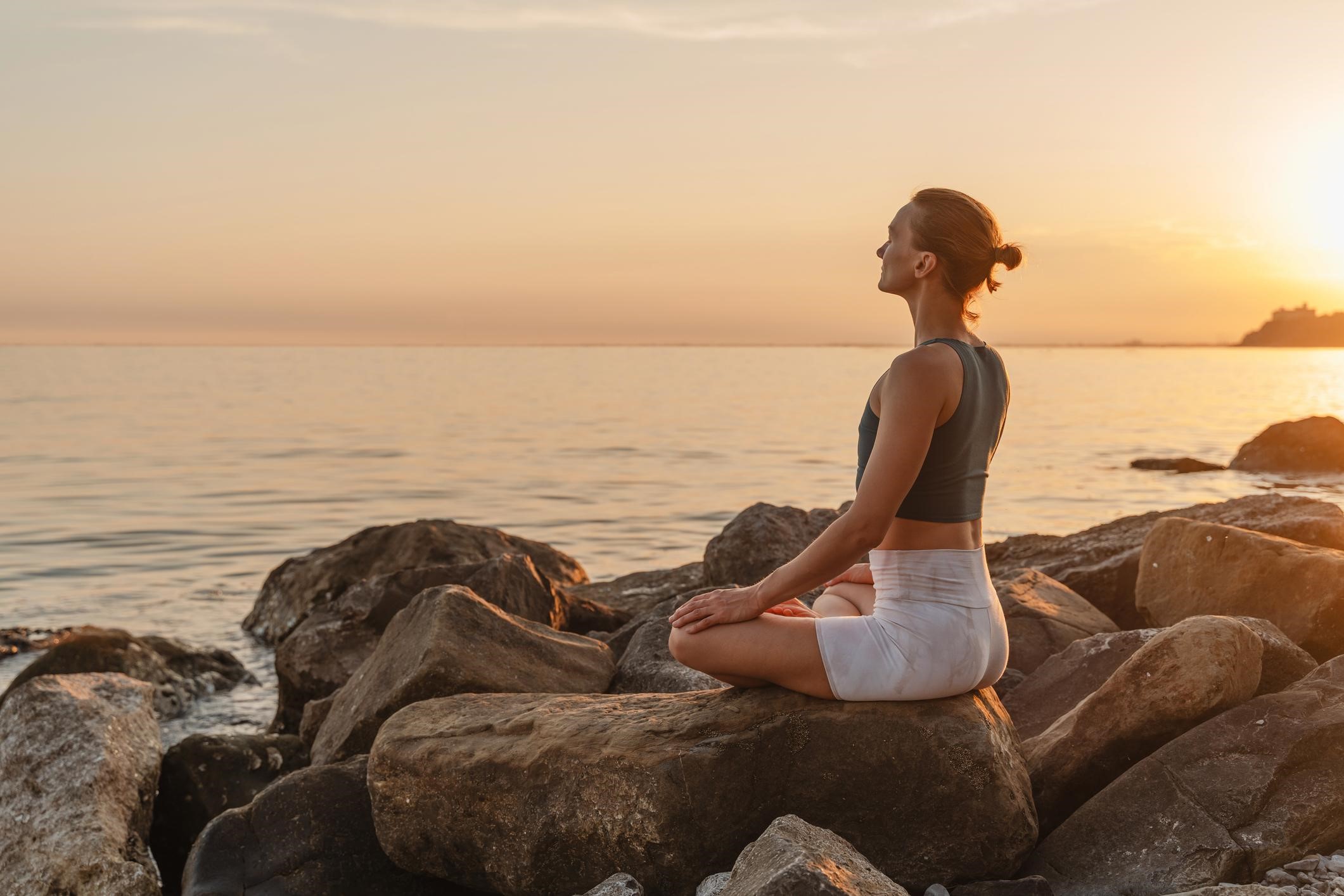 A woman sitting on rocks by the sea at sunrise