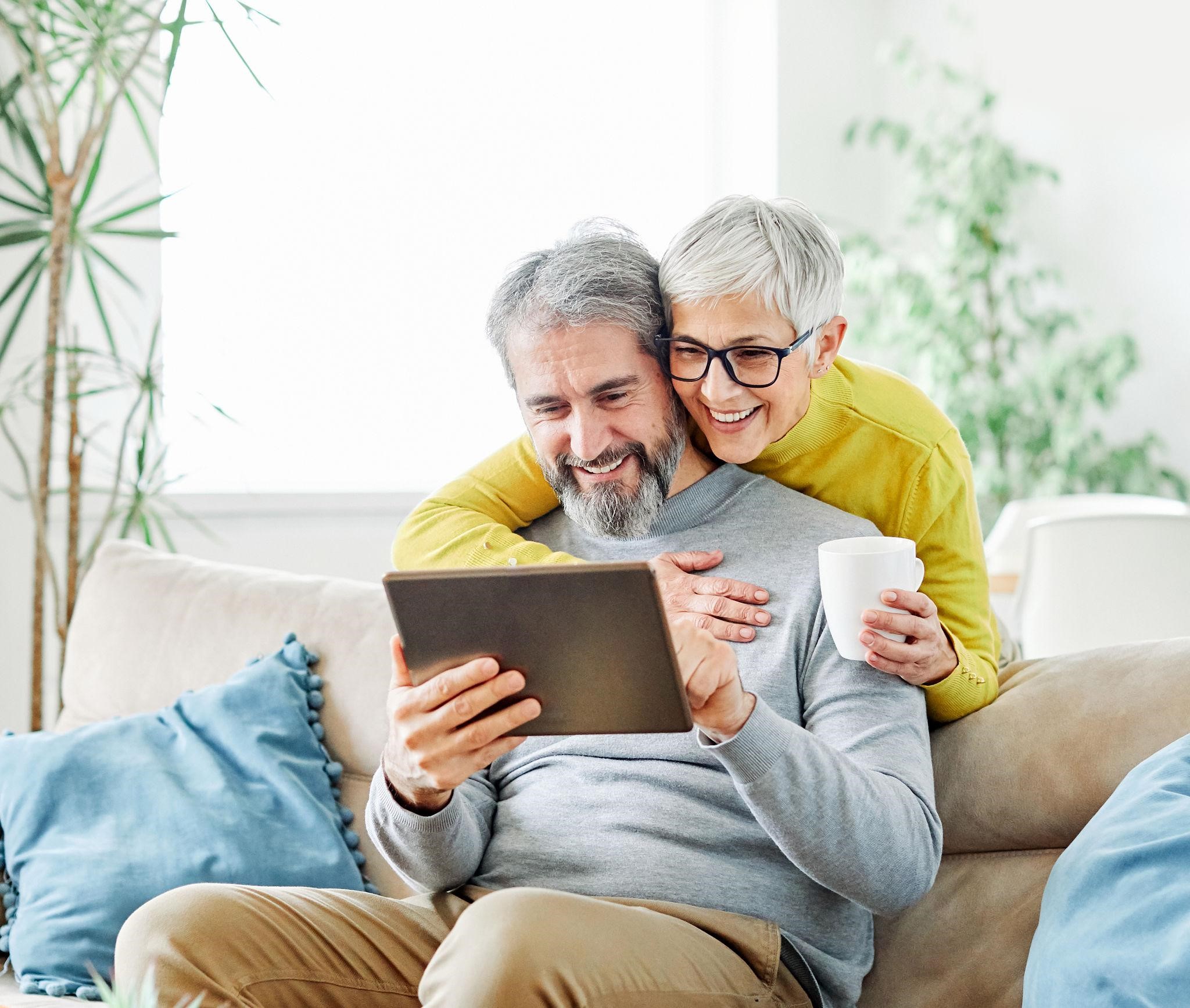 An older couple laughing together while using a voice assistant